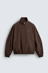 Cazadora técnica de corte boxy fit en color marrón, con cuello subido, cierre frontal de cremallera, bolsillos laterales y uno frontal con cierre, y acabados elásticos en puños y ruedo.