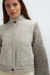 Campera de lana fina color crema, con cuerpo estructurado y mangas de tejido de punto acanalado. Presenta cuello alto, cierre frontal con botones y bolsillos laterales con doble abertura.
