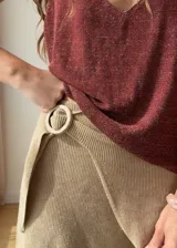Falda corta cruzada de tejido de punto con lurex y viscosa, color negro con destellos dorados. Presenta un diseño envolvente con hebilla decorativa de madera en la cintura.