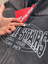 Campera canguro con cierre frontal, capucha y bolsillos tipo canguro, en tono marrón con efecto gastado vintage y estampa gráfica blanca con detalles de strass en el pecho.