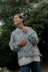 Buzo de tejido de punto calado con diseño de red, cuello redondo y mangas largas abullonadas. Presenta una textura jaspeada en tonos gris y blanco.