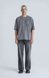 Remera de corte oversize color gris melange, con cuello redondo y mangas cortas. Presenta un estampado en la espalda inspirado en la carta del tarot 'El Mundo', con diseño gráfico detallado y tipografía alusiva.