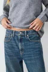 Pantalón jean azul de tiro medio, corte barrel con ajuste relajado en la parte superior, diseño clásico de cinco bolsillos, con cierre frontal de cremallera y botón metálico.