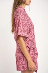 Camisa de manga corta con estampado abstracto en tonos rosa y borgoña. Tiene cuello camisero, cierre frontal con botones y corte oversize.