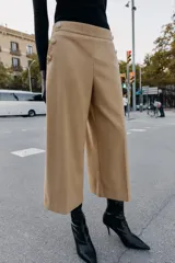 Pantalón tipo culotte de tiro alto, con pernera ancha y corta. Presenta detalles de botones dorados decorativos en la parte frontal y cierre lateral con cremallera oculta.