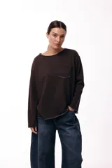 Remera de algodón color marrón oscuro, con corte holgado, escote redondo amplio, mangas largas y bolsillo frontal tipo parche. Presenta terminaciones con efecto desgastado en cuello, puños y ruedo.