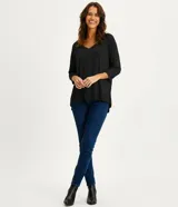 Blusa básica de viscosa color negro, con escote en V y mangas 3/4. Presenta un corte holgado con dobladillo asimétrico, siendo más larga en la parte posterior.
