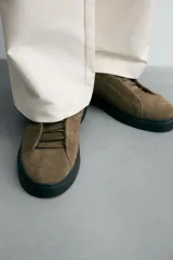 Zapatilla de estilo urbano confeccionada en piel con acabado de serraje. Presenta un diseño minimalista con cordonera oculta y suela de goma a contraste.