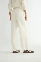 Conjunto de dos piezas tejido en color crema, compuesto por un cárdigan con cierre frontal completo y cuello alto, y pantalón de corte recto con cintura elástica.