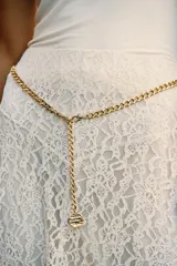 Falda midi color crema o blanco roto, confeccionada en tejido de encaje con forro interior a tono. Presenta cintura elástica y se complementa con un cinturón tipo cadena metálica dorada con caída.