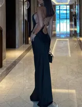 Vestido largo negro de silueta ajustada y escote halter. Presenta espalda descubierta con tiras finas y un aplique metálico con pedrería de strass.