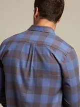Camisa de franela a cuadros azules y grises, de manga larga con puños abotonados y dos bolsillos frontales con solapa abotonada.