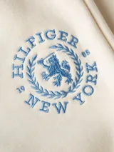 Pantalón de jogging color crema, con cintura elástica y cordón ajustable. Presenta un logo circular con el monograma TH bordado en azul en el muslo.