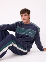 Sweater de cuello redondo marca Rusty, con diseño de bloques de color en azul marino y verde, con detalles de líneas blancas. Presenta el logo de la marca bordado en el pecho.