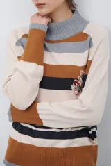 Polera de tejido de punto con diseño de rayas horizontales en tonos beige, marrón, gris y negro. Presenta cuello redondo y mangas largas con puños en contraste.