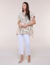 Blusa de silueta holgada confeccionada en crepé liviano, con estampado abstracto en tonos rosados, verdes y blancos. Presenta escote redondo amplio, hombros caídos con hilera de botones decorativos, mangas cortas con dobladillo y ruedo asimétrico en picos.
