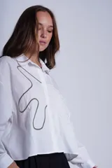 Camisa negra de manga larga con cuello clásico y cierre frontal con botones. Presenta bordados abstractos en blanco y negro en el frente.