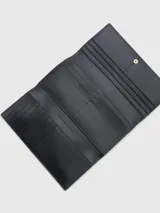 Billetera grande de Tommy Hilfiger en color negro con textura granulada, cierre de botón a presión y monograma TH metálico en tono dorado en la parte frontal.