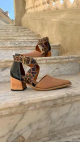 Zapatos de cuero color tostado con puntera fina y taco bloque de madera de 6 cm. Cuentan con tiras cruzadas con estampado animal print de leopardo en el empeine, talón negro y tira al tobillo con hebilla metálica ajustable.