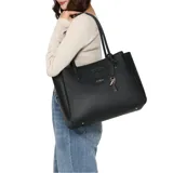 Cartera tipo shopper Guess modelo Isola, color negro con textura granulada. Presenta el logo de la marca en relieve en el frente, asas dobles para hombro y un charm colgante con llaves y placa metálica dorada.