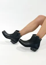 Botas cortas de cuero negro con punta cuadrada y taco bajo de madera. Presentan un detalle de tiento cosido a mano en la parte superior.