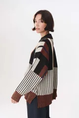 Buzo de tejido de punto con diseño de bloques de rayas verticales en colores rojo, verde, bordó y crema. Presenta cuello alto, corte oversize y terminaciones en rib en puños y ruedo.
