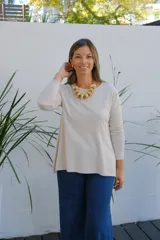Sweater de tejido de punto en color beige, con cuello redondo, mangas tres cuartos y corte holgado con ruedo ligeramente más largo en la parte posterior.
