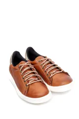 Deportivo de cuero liso color caramelo, con cordones beige y suela blanca. Presenta un detalle metalizado plateado en el talón.