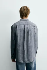 Camisa de corte relajado confeccionada en tejido fluido con mezcla de viscosa, presenta un diseño de rayas verticales, cuello solapa, cierre frontal con botones, manga larga con puño abotonado y un bolsillo de plastrón en el pecho.