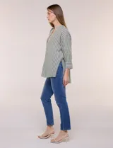 Blusa de silueta holgada a rayas verdes y blancas, confeccionada en tela liviana con textura arrugada. Presenta cuello en V profundo con botones frontales, mangas 3/4 de hombro caído y ruedo asimétrico con aberturas laterales.