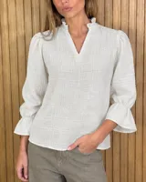 Blusa rosada de algodón con delicados bordados florales blancos, escote en V con cuello elevado y volados, y mangas largas con puños acampanados.