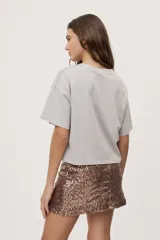 Remera gris de fit amplio, con mangas cortas y cuello redondo. Presenta efecto lavado y estampa frontal con aplicación de strass con la frase "fiesta mode on".
