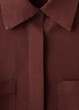 Camisa oversize color borravino, de manga larga con puños abotonados, cuello camisero, dos bolsillos de parche en el frente y cierre delantero con botones.