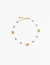 Tobillera de acero color dorado con cadena fina, intercalando dijes de mano Hamsa y cuentas de ojo turco (evil eye) en resina azul y blanca.