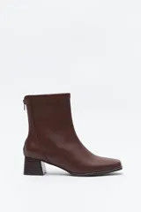 Bota de caña baja de color marrón, con diseño liso, puntera cuadrada, taco medio geométrico y cierre en la parte trasera.