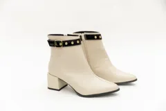 Botas de cuero negro, de caña baja, punta fina y taco cuadrado. Presentan un aplique charolado al tono, una correa con hebilla y ojales metálicos.