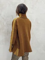 Sweater de punto con patrón de espiga en tonos beige y marrón, cuello alto, mangas largas con detalles en naranja y puños marrones.
