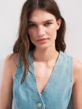 Chaleco de denim con cuello en V, cierre frontal con botones y lazo ajustable en la cintura. Presenta un diseño entallado con costuras verticales y bajo redondeado.