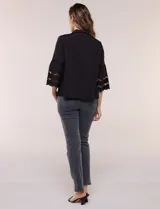 Camisa negra de poliéster con cuello camisero, escote en V y cierre frontal de botones. Cuenta con mangas anchas de corte acampanado y detalles de bordado suizo calado en las mangas y en el ruedo inferior.