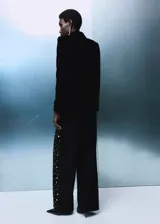 Jeans rectos de tiro medio en tejido de algodón vaquero color negro, con diseño de cinco bolsillos, trabillas para cinturón y cierre frontal con botón y cremallera. Presenta aplicaciones de tachuelas brillantes a lo largo de las piernas.