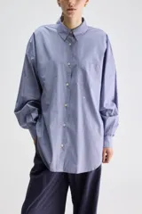 Camisa de silueta oversize de algodón color celeste, con cuello clásico, cierre frontal con botones, hombros caídos, bolsillo aplicado en el pecho y puños abotonados.