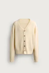 Cárdigam relaxed fit de punto tejido en color beige claro, con cuello en V, manga larga, acabados en rib y cierre frontal de botonadura con botones en tono carey.
