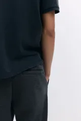 Pantalón tipo jogger de punto en tono gris oscuro, con cintura elástica y cordón ajustable. Presenta un pliegue cosido en el frente de cada pierna, bolsillos laterales y un bolsillo insertado trasero.