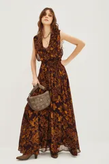 Vestido largo sin mangas con escote en V profundo y lazo ajustable en la cintura. Presenta un estampado geométrico en tonos marrón y ocre sobre fondo oscuro, con falda amplia y fluida.