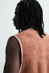 Camiseta tank (sin mangas) de corte relajado, color terracota con efecto lavado y estampado frontal de estrellas en blanco. Presenta cuello redondo y acabados deshilachados en las sisas y el ruedo.