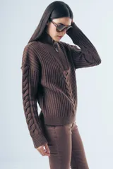 Sweater de punto grueso color azul marino, con cuello polo y cierre frontal parcial. Presenta un diseño de tejido trenzado en el centro y mangas largas con puños acanalados.