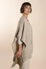 Ruana color crema tejida en punto fantasía con efecto de volado en los bordes.