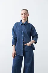 Sobrecamisa de jean negra de silueta relajada, con tachas aplicadas en líneas orgánicas que recorren la prenda. Tiene cuello camisero, cierre frontal con botones a presión y mangas largas.