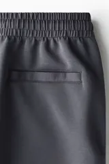 Short de felpa interlock color gris oscuro, con cintura elástica fruncida y cordón ajustable. Presenta un diseño de corte relajado a la rodilla, bolsillos laterales y bolsillos traseros.