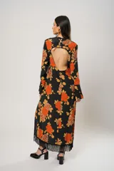 Vestido largo negro con estampado de flores naranjas y amarillas, cuello mao con abertura en forma de gota, mangas largas acampanadas con botones en los puños, tajo lateral y flecos en el ruedo.